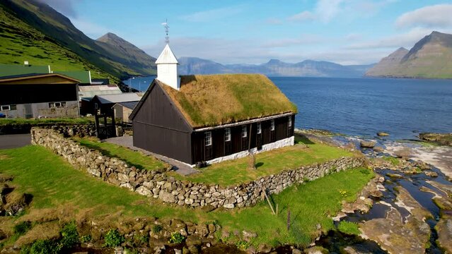 FAROE ISLANDS - JULY.16.2023 - Excellent aerial view tilting up a chapel with a grassy roof on the coast of Funningur in the Faroe Islands.