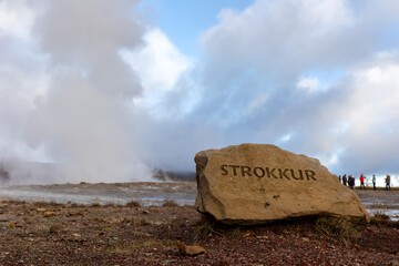 icelandic geyser erupting high in the air with rock with the name of the geyser
