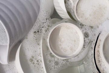 Dishes and bowls in water and bubbles of dishwashing liquid. Kitchen work