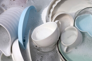 Dishes and bowls in water and bubbles of dishwashing liquid. Kitchen work