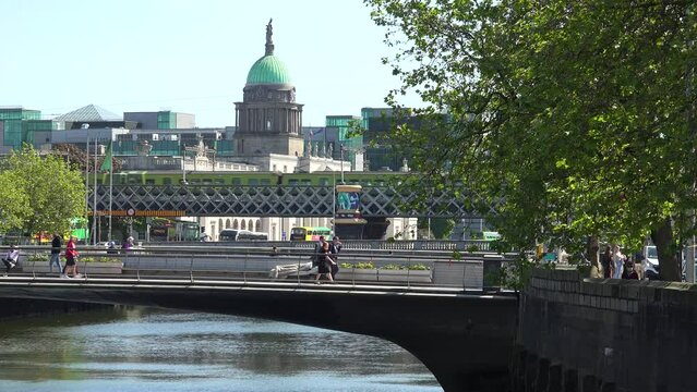 DUBLIN - JULY.27.2023 - People cross the Rosie Hackett Bridge over the River Liffey in Dublin, Ireland, passing the Custom House on a sunny day.