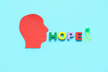 Paper human head with green awareness ribbon and word HOPE made of wooden letters on blue background. Mental Health Day