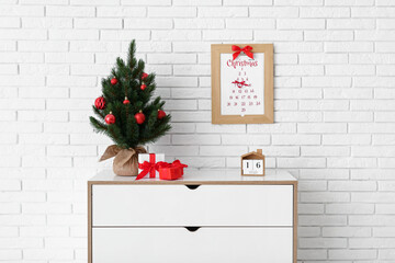 Christmas tree with presents and calendar on drawers in room