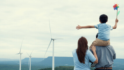 Concept of progressive happy family enjoying their time at the wind turbine farm. Electric generator from wind by wind turbine generator on the country side with hill and mountain on the horizon. © InfiniteFlow
