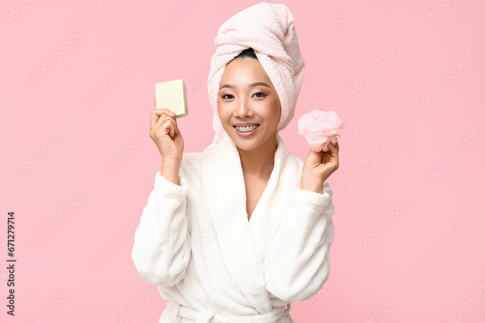 Sticker Young Asian woman with soap and loofah on pink background