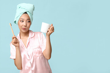 Young Asian woman with toothbrush and cup on blue background