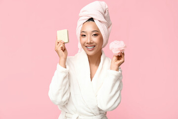 Young Asian woman with soap and loofah on pink background