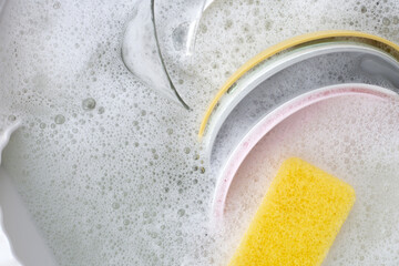 Dishes and bowls in water and bubbles of dishwashing liquid. Kitchen work
