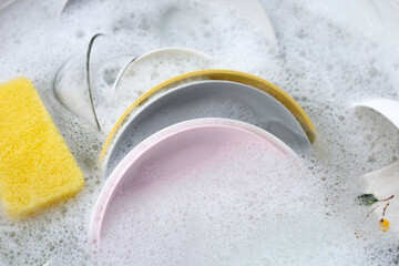 Dishes and bowls in water and bubbles of dishwashing liquid. Kitchen work