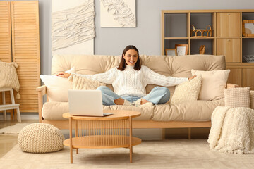 Young woman in warm sweater sitting on sofa at home