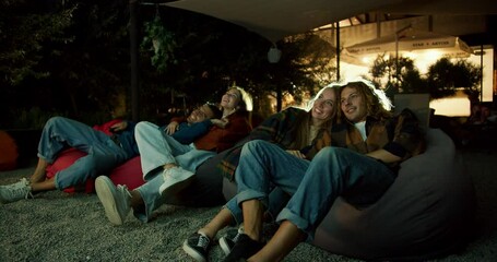 Two couples in love are sitting on beanbag chairs and watching a movie. A party outside the city. Rest in the country house