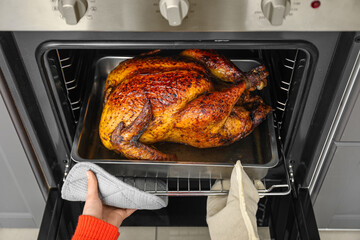 Woman taking tasty baked turkey from oven in kitchen. Thanksgiving Day celebration