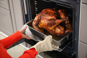 Woman taking tasty baked turkey from oven in kitchen. Thanksgiving Day celebration