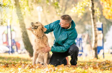 Man playing with his dog golden retriever in autumn park