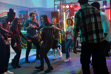 People partying in nightclub while having fun and dancing on dancefloor with spotlights together. Young men and women crowd attending discotheque and music concert in club