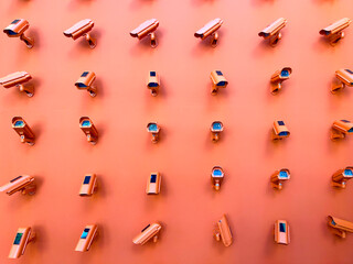 Horizontal photography of a bunch of CCTV cameras pointing in all directions mounted on an orange wall.  - obrazy, fototapety, plakaty