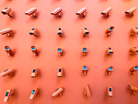 Horizontal photography of a bunch of CCTV cameras pointing in all directions mounted on an orange wall. 