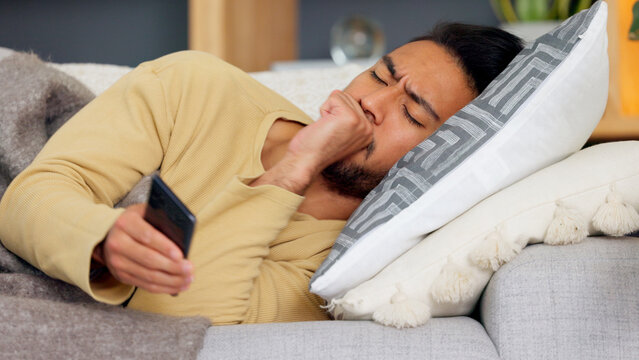 Man, phone and cough on sofa in home living room, texting or communication with email notification. Guy, smartphone and sick with research for health, medicine or watch video on social media in house