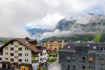 Early morning terrace balcony view of the Swiss Alps and illuminated town of Engelberg, Switzerland, as clouds break and the mountains appear through fog near Mt Titlis.
