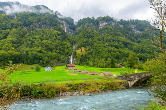 An Alpine stream runs under an old stone bridge past a small village at the base of Fallenbach Waterfall, or Fallenbachfalle near Engelberg and Wolfenschiessen in the Obwalden region of Switzerland.