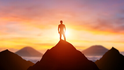 Fototapeta na wymiar Silhouette of a business person on the top of a mountain peak in sunset background. Winner and conquer of businessman concept.
