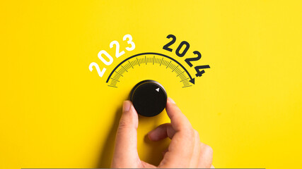 Close up of a hand adjusting volume button from year 2023 to 2024 on isolated yellow background. Happy New Year celebration concept. - obrazy, fototapety, plakaty