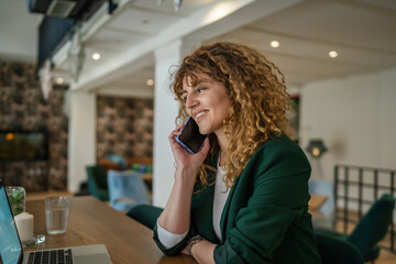 Woman use smartphone make a call talk while work on laptop from cafe