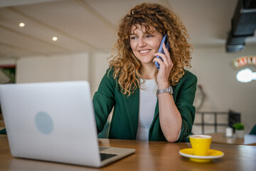 Woman use smartphone make a call talk while work on laptop from cafe