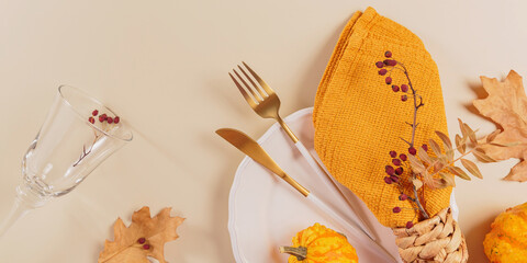 Autumn table setting with pumpkin decorations on light background. Empty plate, glass, cutlery, yellow napkin and dry leaves. Autumn holiday mood, Halloween, Thanksgiving concept. Top view, flat lay