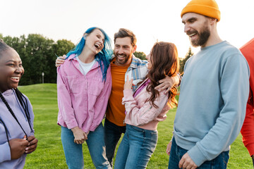 Group of happy stylish multiracial friends wearing colorful clothing laughing, having fun, hangout on corporate party in park. Diversity, friendship, positive lifestyle  concept 