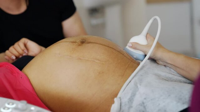 Doctor's hand moving ultrasound transducer by the big pregnant belly of an unrecognized woman. Checking the pregnancy on the last stages before baby delivery.