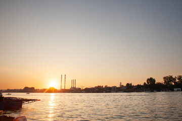 Panorama of the reka Sava river in belgrade, in Serbia, with a Industrial landscape of Eastern Europe with red and white factories and chimneys polluting, at dusk, during a sunny afternoon.