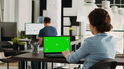 Businesswoman looks at greenscreen on laptop, checking pc at desk and working on startup operations. Employee using isolated chromakey template on computer, copyspace display.