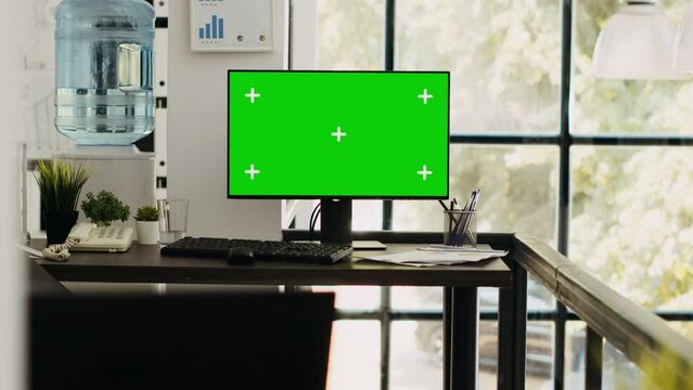 Modern coworking space with monitor showing isolated greenscreen, blank chromakey screen on computer. Empty office desk with pc running mockup template, copyspace layout on desktop.