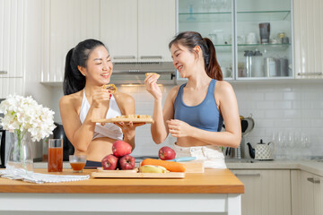 Two healthy Asian female friends in exercise clothes  Is happily cooking a healthy meal in her home...