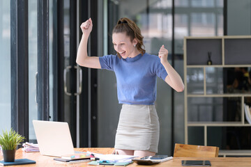 Happy businesswoman laughing with joy at the good news about work at the workplace, gladly looking at laptop screen, feeling excited.