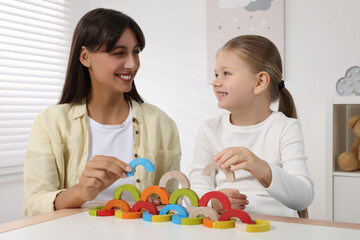 Motor skills development. Mother helping her daughter to play with colorful wooden arcs at white table in room