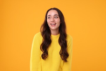 Beautiful young woman in stylish warm sweater on orange background