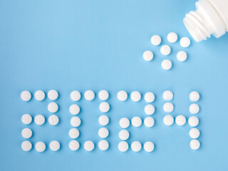 2024 Happy New Year banner for health care and medical concept. Number 2024 made from tablets, tablets blow out or ejection from bottle on blue background. View from above flat lay. Medical concept