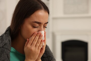 Sick woman wrapped in blanket with tissue blowing nose at home, closeup and space for text. Cold...