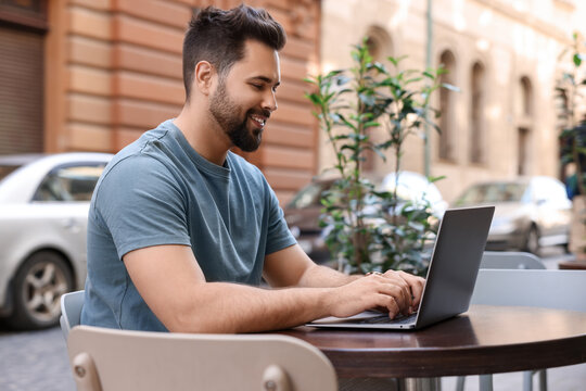 Handsome young man working on laptop at table in outdoor cafe