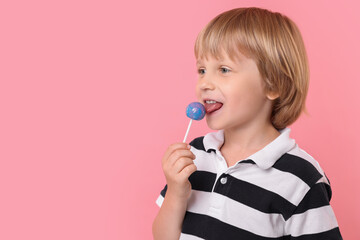 Cute little boy licking lollipop on pink background, space for text