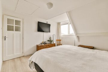 a bedroom with white walls and wood flooring the room has a flat screen tv mounted on the wall above the bed