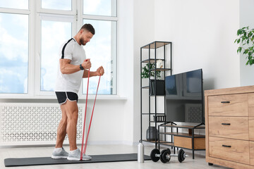Fototapeta na wymiar Athletic man doing exercise with elastic resistance band on mat at home