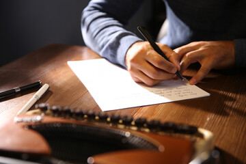 Man writing letter at wooden table indoors, closeup
