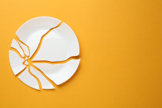 Pieces of broken ceramic plate on orange background, flat lay. Space for text
