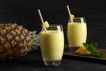 Tasty pineapple smoothie and fruit on black table