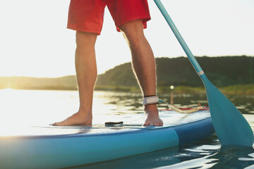 Man paddle boarding on SUP board in river at sunset, closeup