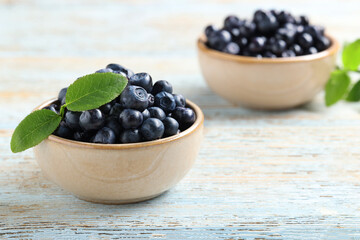 Tasty fresh bilberries with leaves on old light blue wooden table, space for text