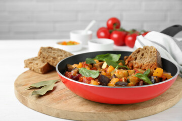 Dish with tasty ratatouille, bread and basil on white wooden table